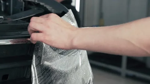 Detailer worker installing wet PPF or Paint Protection Film on Car Headlight for Stock Footage 150903624