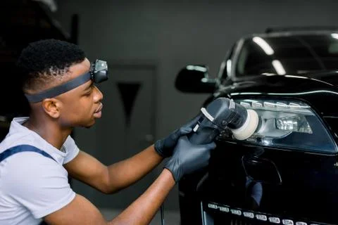 Detailing and polishing of car headlight. Young dark skinned worker in uniform Stock Photos