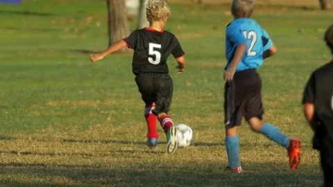 Details of a ball and boys legs playing youth soccer football on a green field. Stock Footage