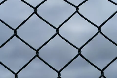 Details of a wire-mesh fence in front of the dark and cloudy sky - security c Stock Photos