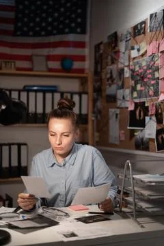 Detective processing evidence in her office, looking on killers photos Stock Photos