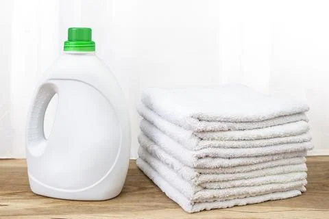 Detergent bottle with blank labels next to stacks of white towels on oak wo.. Stock Photos