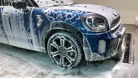 Detergent foam flows down from blue car at carwash service Stock Footage 194229595