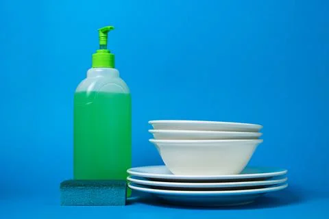 Detergent next to clean plates on a blue background. Stock Photos