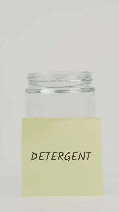 Detergent text or word on yellow sticky note attached to glass jar with hand Stock Footage 311713901