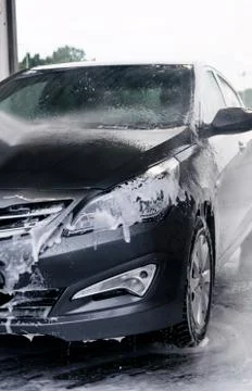 Detergent is washed off the front of a gray car with water Stock Photos