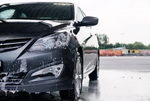 Detergent is washed off the front of a gray car with water Stock Photos