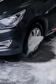 Detergent is washed with water from the front wheel of a gray car at the sink Stock Photos