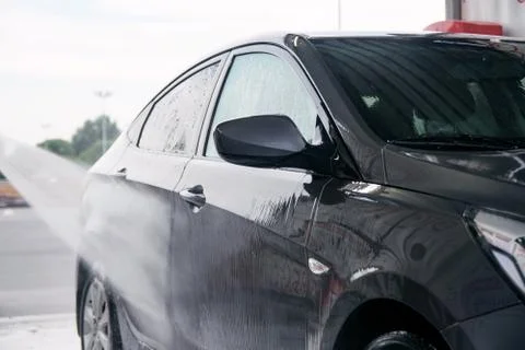 Detergent is washed off with water from the side of the gray car at the sink Stock Photos