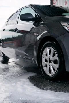 Detergent is washed off with water from the side of the gray car at the sink Stock Photos