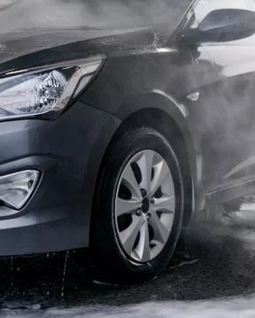 Detergent is washed off with water from the side of the gray car at the sink Stock Photos