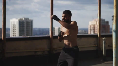 Determined Black male fighter practicing shadow boxing on high-rise rooftop Video stock 331073090