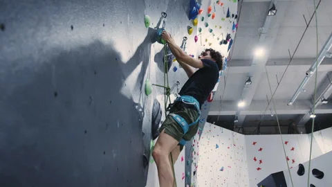 Determined Climber Scaling Vertical Wall with Green Holds in Modern Indoor Stock Footage 276999661