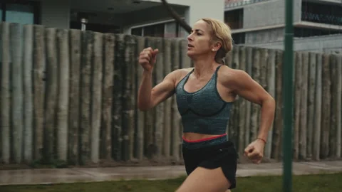 Determined female runner sprinting past wooden fence on cloudy morning Stock Footage 339621640