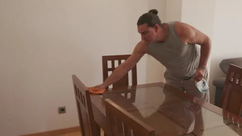 Determined man cleaning a glass table at home Stock Footage 340074214