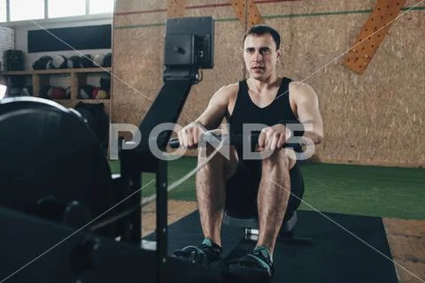 Determined man exercising on rowing machines at gym Stock Photos