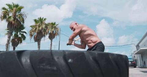 Determined man hitting wheel tyre with sledge hammer Stock Footage 116384123