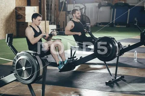 Determined men exercising on rowing machines at gym Stock Photos