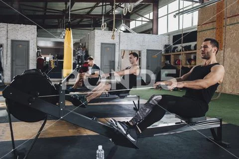 Determined men exercising on rowing machines at health club Stock Photos