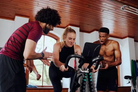Determined multiracial young adults clapping for friend on exercise bike at the Stock Photos