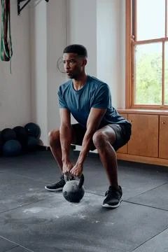 Determined muscular young black man doing kettlebell squats at the gym Stock Photos
