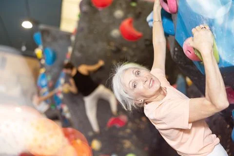 Determined old lady doing difficult wall climb in climbing gym Stock Photos