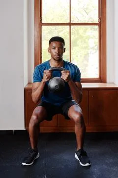 Determined young black man doing kettlebell squats at the gym Stock Photos