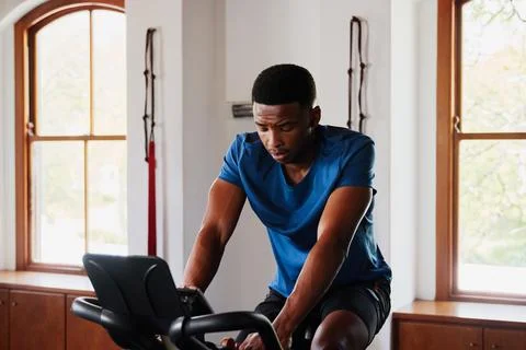 Determined young black man doing cardio workout on exercise bike at the gym Stock Photos