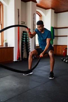Determined young black man doing workout with battle ropes at the gym Stock Photos