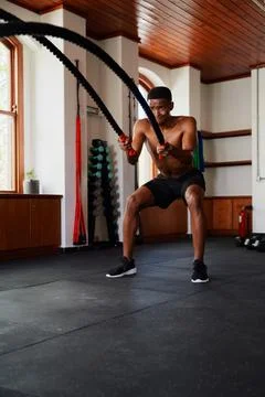 Determined young black man doing battle ropes exercises at the gym Stock Photos