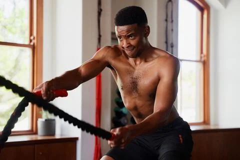 Determined young black man exercising with battle ropes at the gym Stock Photos