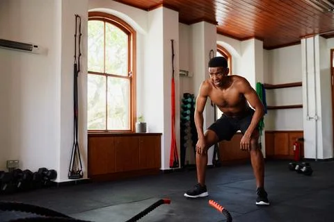 Determined young black man taking a break by battle ropes at the gym Stock Photos