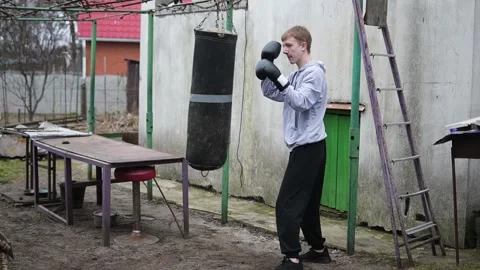 Determined Young Man in Boxing Gloves Training Outdoors with Heavy Punching Bag Stock Footage 339766289