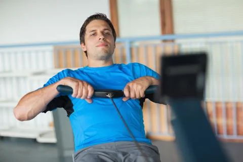 Determined young man working out on row machine Photos