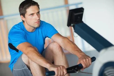 Determined young man working out on row machine Stock Photos