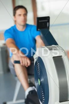 Determined young man working out on row machine Stock Photos