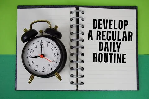 Develop A Regular Daily Routine text written on notebook paper with alarm clo Foto stock
