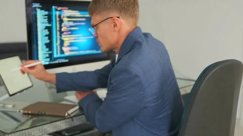 Developer analyzes code on computer, optimizing tasks with tablet. Stock Footage 294299036