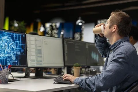 Developer drinking coffee in office, reviewing AI system metrics Stock Photos