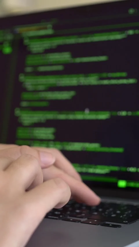 Developer interacts with laptop displaying green code interface. Automation Stock Footage 345654390