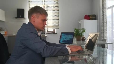 Developer in jacket codes on laptop, workspace bright with green plants. Video stock 294173910