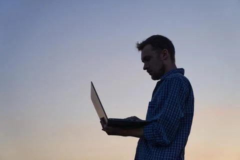 Developer male in silhouette using laptop outdoor at sunset, working Stock Photos