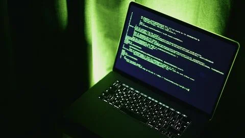 Developer sitting at computer with green backlighting and entering computer code 写真素材