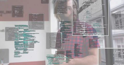 Developer typing code at office desk wearing red flannel shirt with monitor and 库存照片