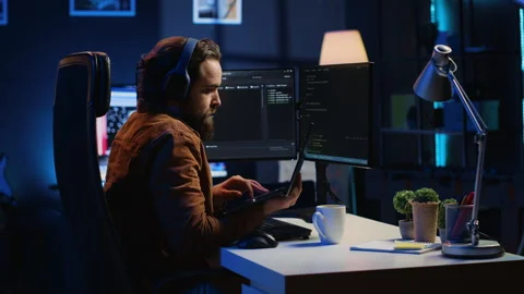 Developer typing complex code in neon lit home office, listening music Stock Footage 265512132