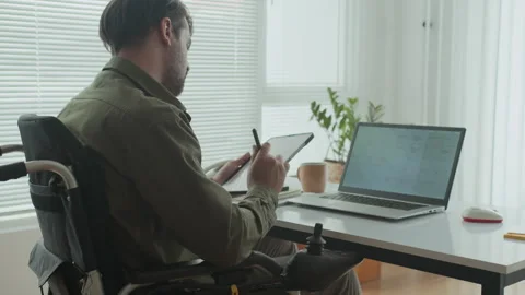 Developer in Wheelchair Using Tablet when Sitting in front of Laptop at Office Video stock 291818545