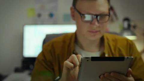 Developer. Young man in home office works intently with electronic tablet at Stock Footage 281106954