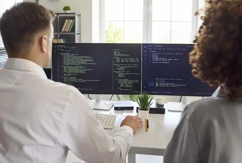 Developers collaborating on code at dual monitors in office, programming team Stock-Fotos