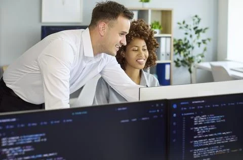 Developers collaborating at computer screens in modern office, coding and 写真素材
