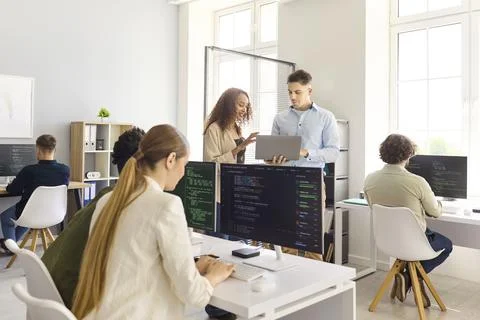 Developers collaborating in modern office, coding at desktops and laptop Stock Photos
